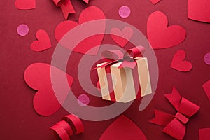 Happy st. Valentines day concept with craft paper gift box, red paper hearts, bows against dark red background with empty space