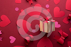 Happy st. Valentines day concept with craft paper gift box, red paper hearts, bows against dark red background with empty space
