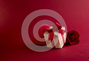 Happy st. Valentines day concept with craft paper gift box, red paper hearts and fresh rose against dark red background with space