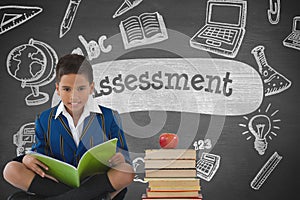 Happy student boy at table reading against grey blackboard with assessment text and education and sc