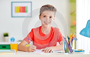 Happy student boy writing to notebook at home