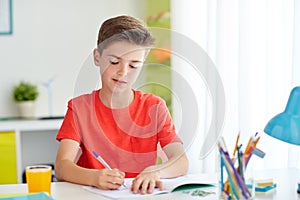 Happy student boy writing to notebook at home