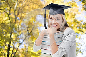 Happy student girl in bachelor cap with books