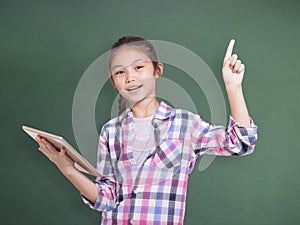 Happy student girl holding tablet and pointing upside.Isolated on green chalkboard background