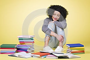 Happy student girl reading surrounded by colorful books.