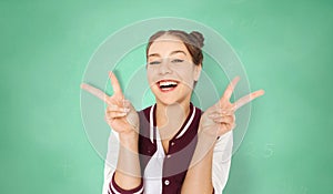 Happy student girl showing peace sign over green