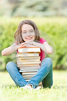 Happy student girl sitting near pile of books