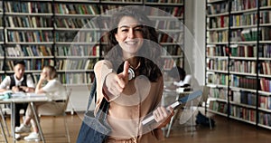 Happy student girl standing in campus library showing thumbs up