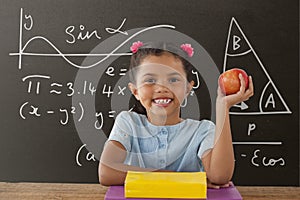 Happy student girl at table holding an apple against grey blackboard with education and school graph