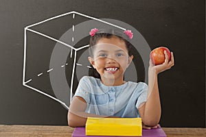 Happy student girl at table holding an apple against grey blackboard with school and education graph