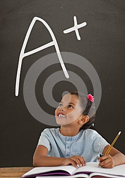 Happy student girl at table looking up against grey blackboard with A+ text