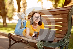 Happy Student Girl Using Laptop Lying On Bench Outdoor