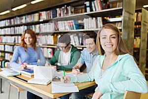 Happy student girl writing to notebook in library