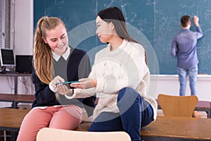 Happy student girls with phone in schoolroom