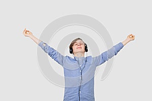 Happy student listening to music with arms raised in air over white background. Young boy student relaxing  listening  to music