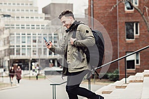 Happy student man text on cell phone walking in city college campus with backpack. photo