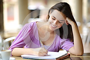 Happy student taking notes in a terrace