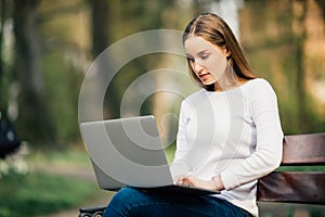 Happy student teenager girl learning with a laptop lying in a bench in an university campus