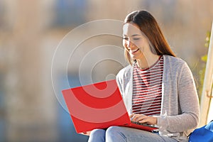 Happy student using red laptop sitting in a campus