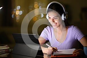 Happy student using tablet and headphone in the night