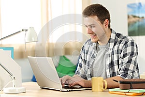 Happy student writing in a laptop in his room