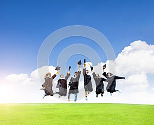 Happy  students in graduation gowns celebrating and jumping  on the grass field
