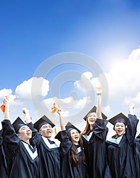 Happy  students in graduation gowns holding diplomas on cloud background