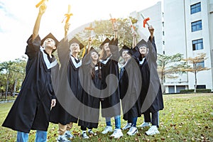 Happy  students in graduation gowns holding diplomas on university campus