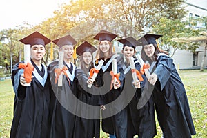 Happy  students in graduation gowns holding diplomas on university campus
