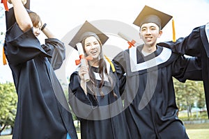 Happy students in graduation gowns holding diplomas on university campus