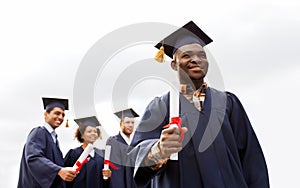 Happy students in mortar boards with diplomas