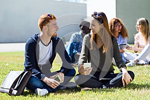 Happy students sitting outside on campus at the university.
