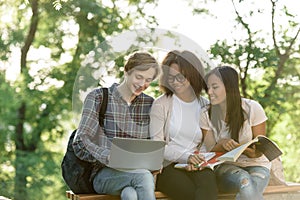 Happy students sitting and studying outdoors while using laptop