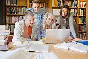 Happy students using laptop at desk in library