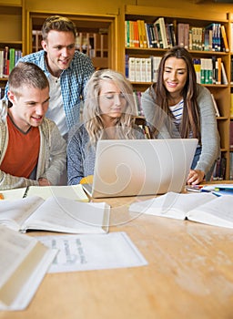 Happy students using laptop at desk in library