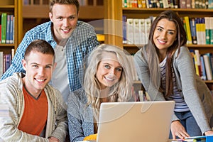 Happy students using laptop at desk in library