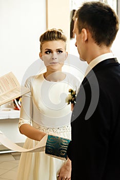 Happy stylish bride and elegant groom exchanging vows at catholic wedding ceremony at church