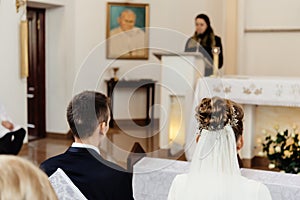 Happy stylish bride and elegant groom sitting at catholic wedding ceremony at church
