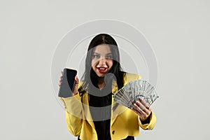 Happy stylish business woman in yellow suit show dollar money isolated on grey