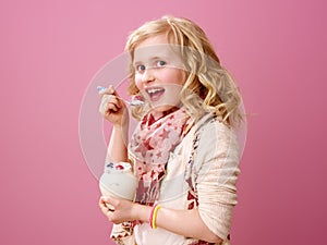 Happy stylish child isolated on pink eating farm organic yogurt