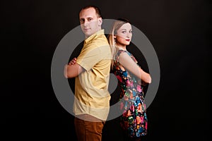 Happy stylish couple standing back each to other in confident pose on black background