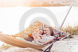 Happy stylish family with cute daughter relaxing in hammock on summer vacation in evening sun light on the beach. hipster couple