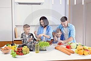 Happy stylish family having fun while preparing healthy vegetables breakfast in modern bright kitchen together.