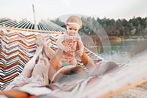 Happy stylish family playing with cute daughter, relaxing in hammock on summer vacation in evening sun light on the beach. hipster