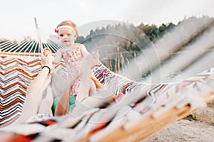 Happy stylish family playing with cute daughter, relaxing in hammock on summer vacation in evening sun light on the beach. hipster