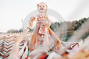 Happy stylish family playing with joyful daughter and cuddling, relaxing in hammock on summer vacation in sun light on the beach.