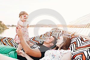 Happy stylish family relaxing in hammock on summer vacation in evening sun light on the beach. hipster couple with child resting
