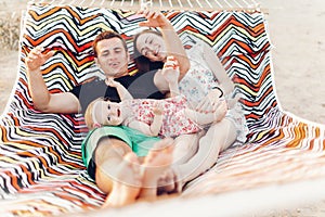 Happy stylish family relaxing in hammock on summer vacation in evening sun light on the beach. hipster couple with child resting