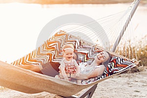 Happy stylish family relaxing in hammock on summer vacation in evening sun light on the beach. hipster couple with child resting