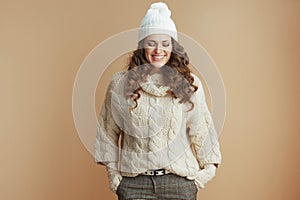 happy stylish female in beige sweater, mittens and hat on beige